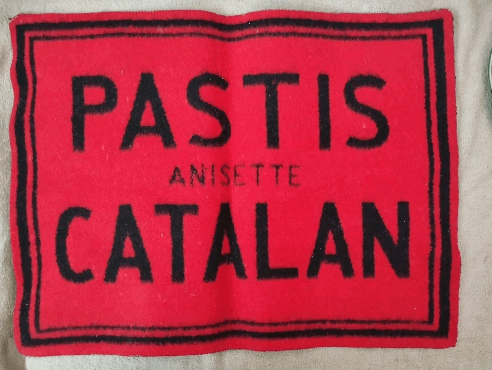 Tapis de comptoir publicitaire « Pastis Anisette Catalan », en feutre rouge et noir (annonce eBay archivée).